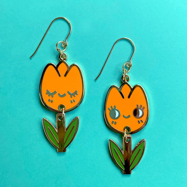Orange tulip-shaped earrings with green leaves on a turquoise background