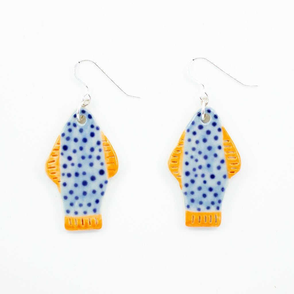 Closeup picture of the Umi earrings, with sterling silver hooks and ceramic beads. Handmade and hand painted ceramic beads are fish shaped, with orange fins and tail, and blue coloured body with polka dots. 