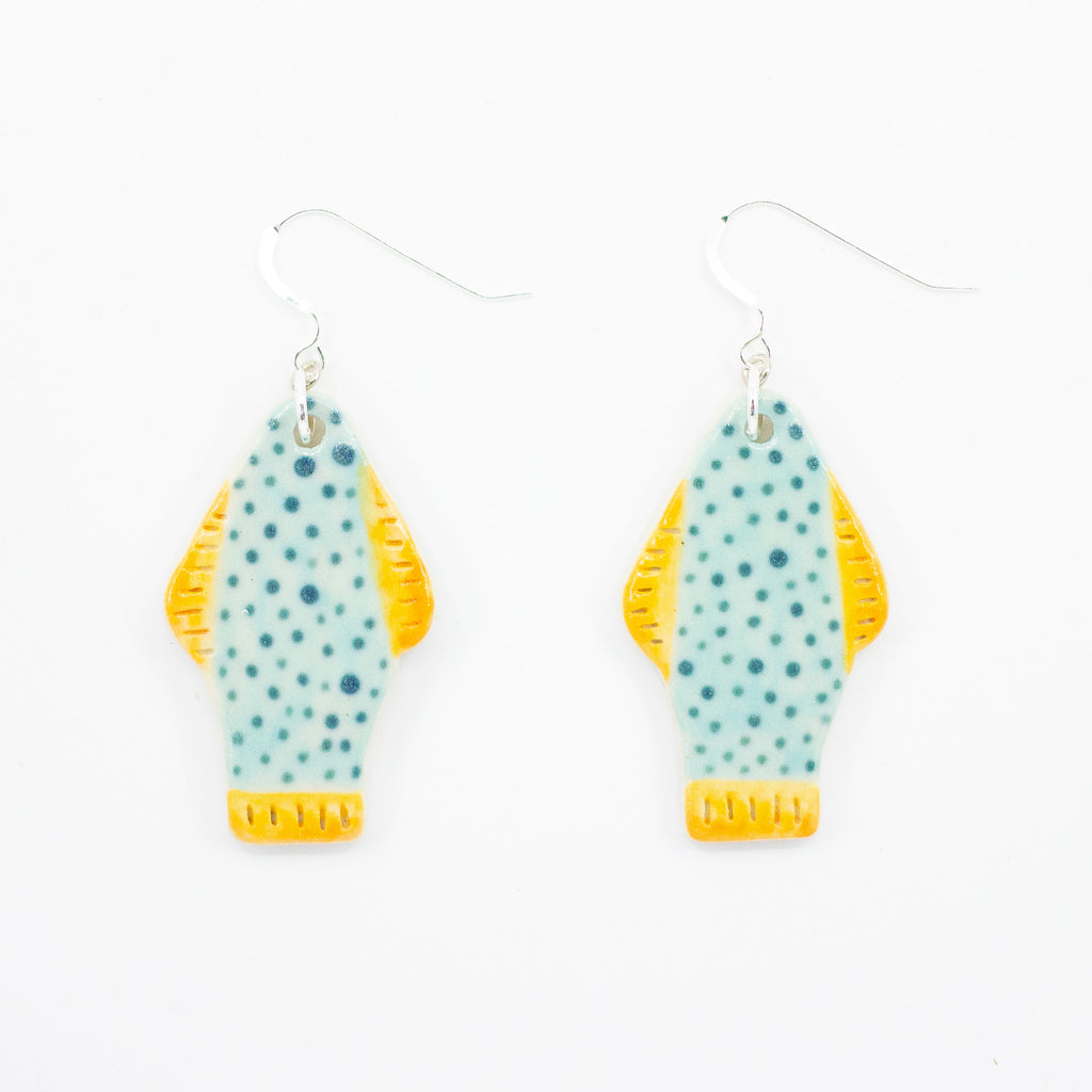 Closeup picture of the Umi earrings, with sterling silver hooks and ceramic beads. Handmade and hand painted ceramic beads are fish shaped, with yellow fins and tail, and teal coloured body with polk dots. 