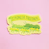 A die-cut sticker featuring a yellow banner that reads 'STRONGER TOGETHER' above green ants, shown on a solid pink background.