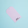 A lilac paper gift tag with a hanging hole and black printed text reading 'shuh.' and 'www.shuhlee.com'