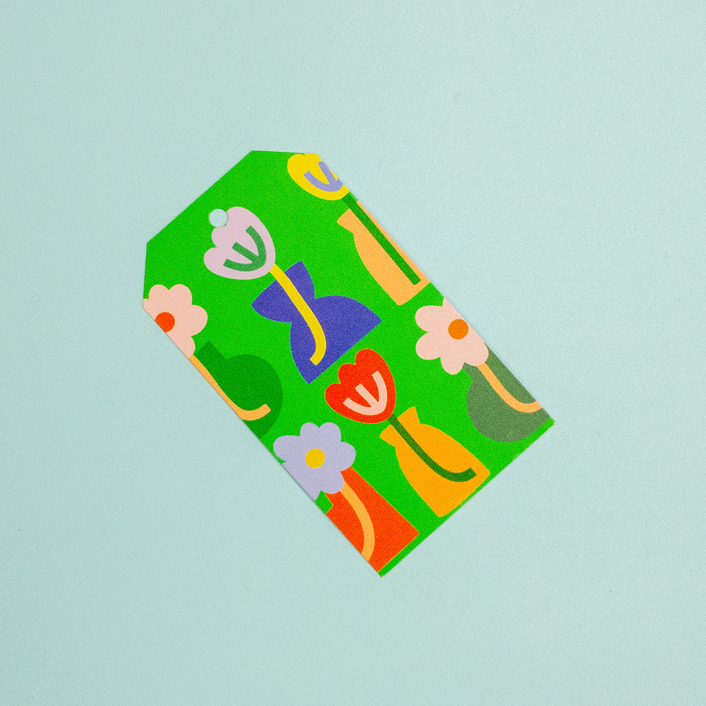 A green paper gift tag with a abstract floral pattern, shown diagonally on a solid light blue background.