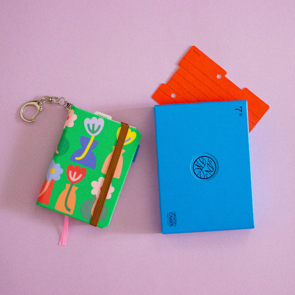 Colorful keychain with a small notebook and blue box on a lilac background
