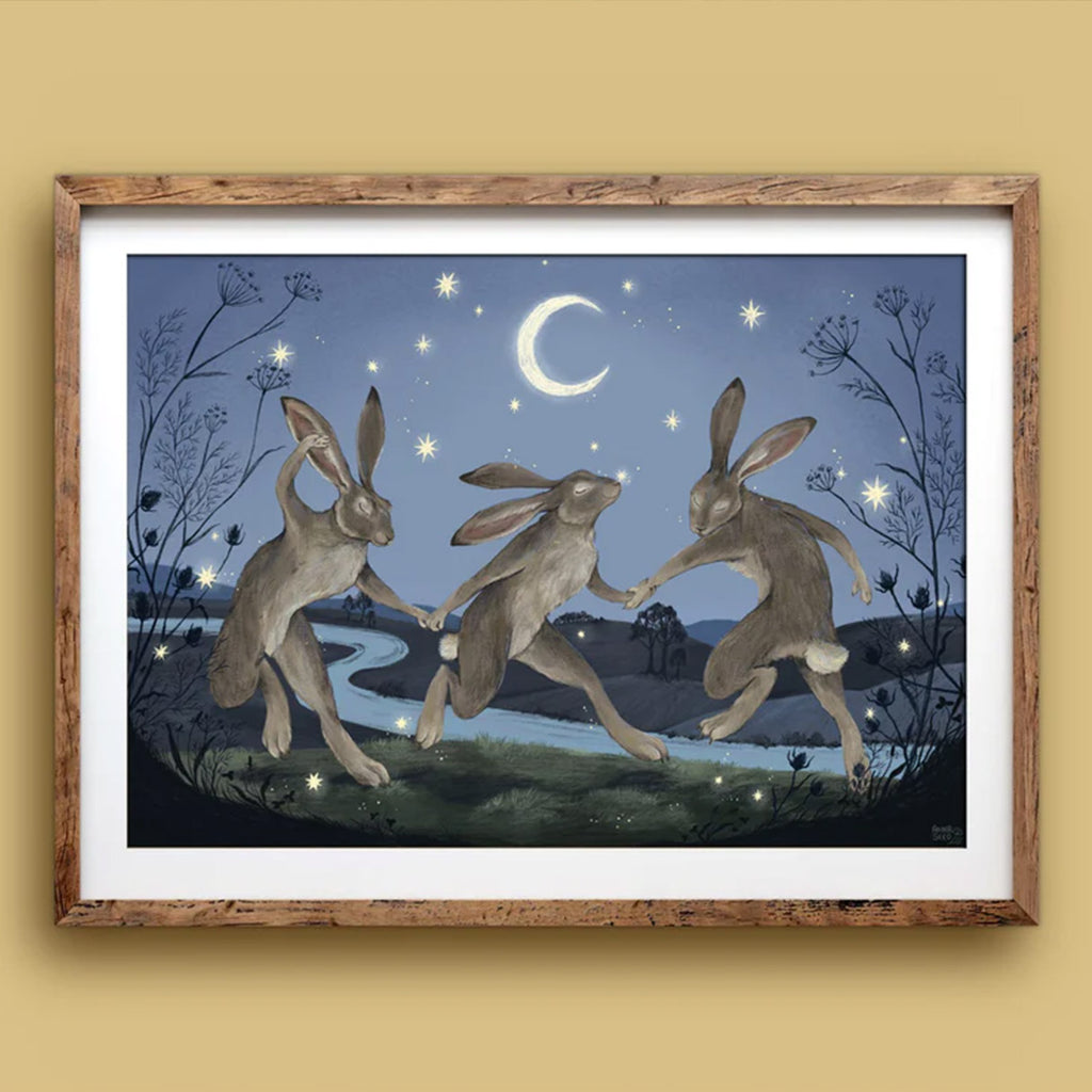 Framed artwork of three hares dancing under a moonlit sky with stars.