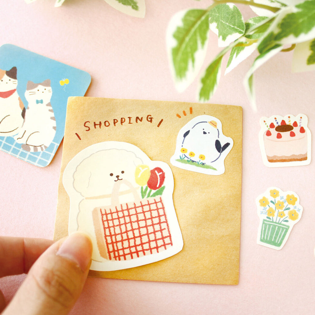 Set of cute stickers on a pink surface with a hand holding a card featuring a sticker.