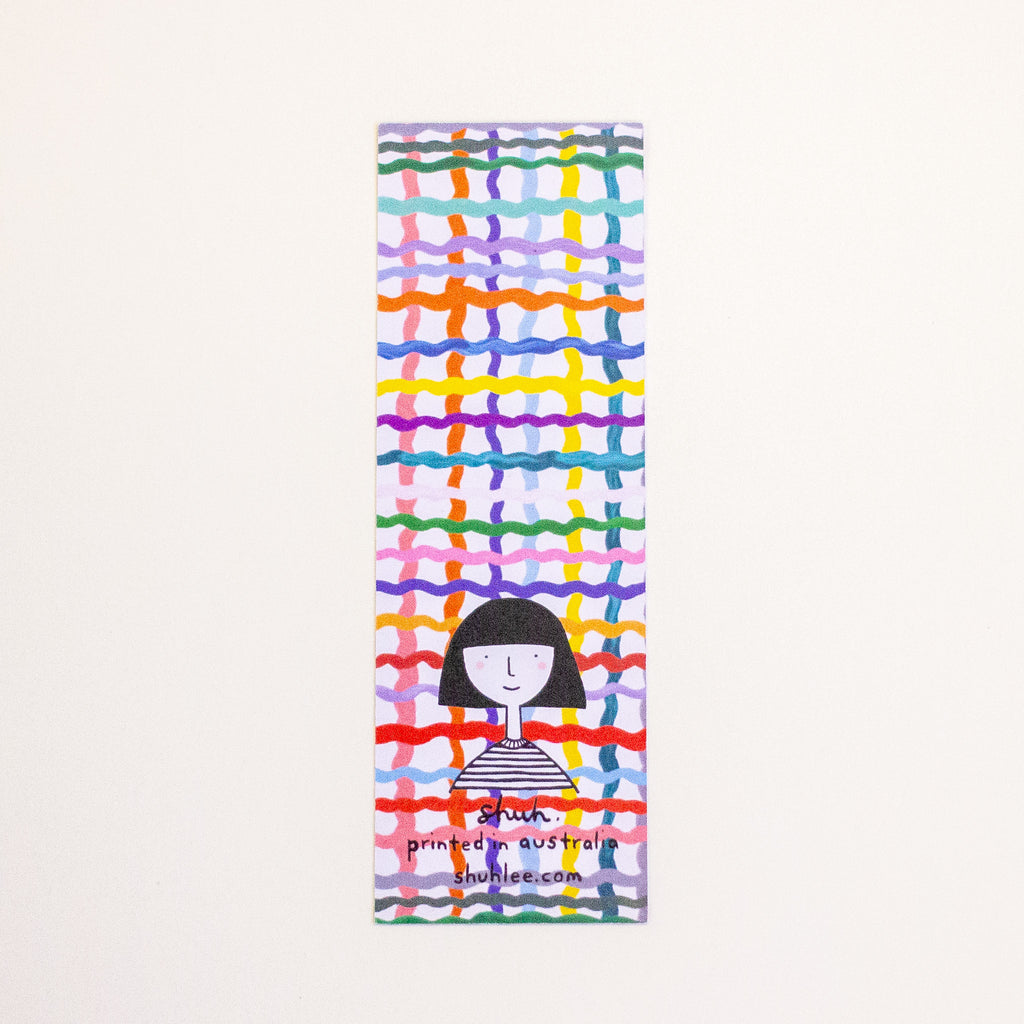 A tall, narrow bookmark with a colourful abstract grid pattern and a simple illustration of a girl near the bottom. The text reads 'shuh. printed in australia shuhlee.com'