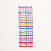 A long, narrow bookmark with a colourful abstract grid and wavy stripe pattern on a white base, shown against a plain off-white background.