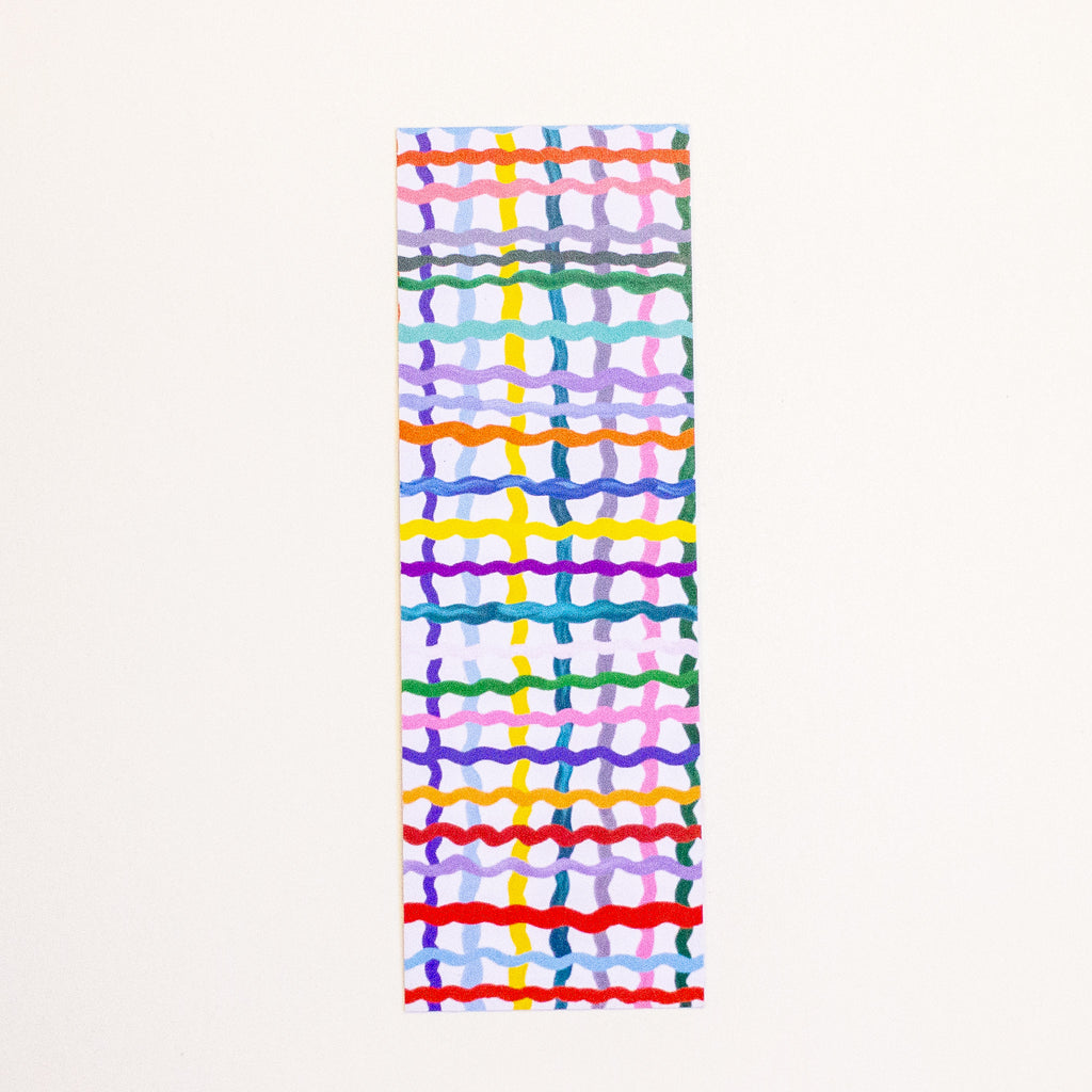 A long, narrow bookmark with a colourful abstract grid and wavy stripe pattern on a white base, shown against a plain off-white background.