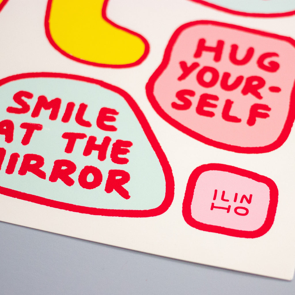 A close-up of a print featuring colourful speech bubbles with text including 'SMILE AT THE MIRROR', 'HUG YOURSELF', and 'ILIN HO'.