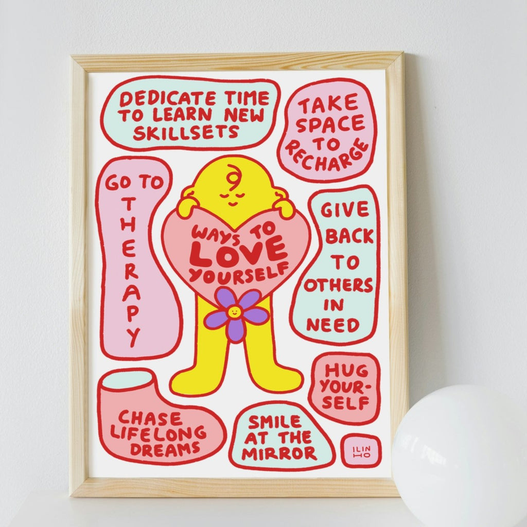 A framed art print with a light wood frame, featuring a yellow cartoon figure holding a pink heart with the words 'Ways to Love Yourself' in red text, surrounded by supportive phrases on a white background.