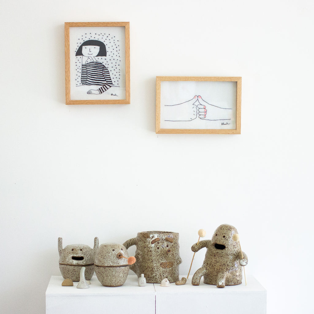 A picture of the doink figurine in context at the well wishes exhibition. Underneath 2 original artworks and between another 3 stoneware artworks. 
