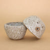 Speckled ceramic figurine and container, separated, on a beige background
