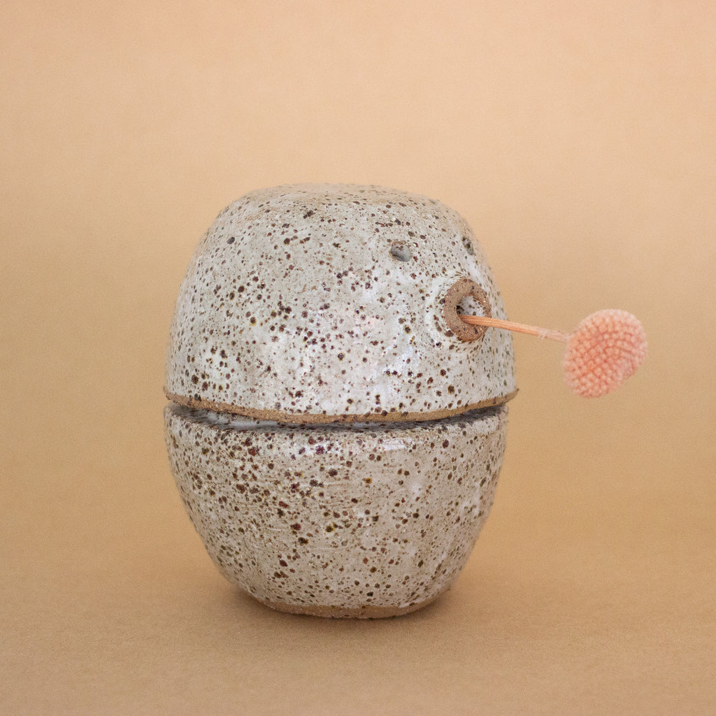 Speckled ceramic container holding a pink flower, on a beige background