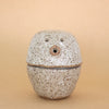 Speckled ceramic figurine and container on a beige background