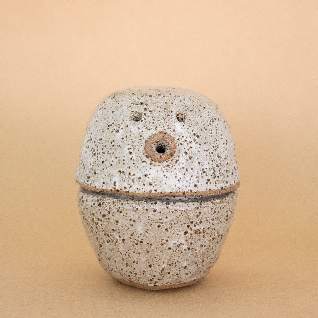 Speckled ceramic figurine and container on a beige background