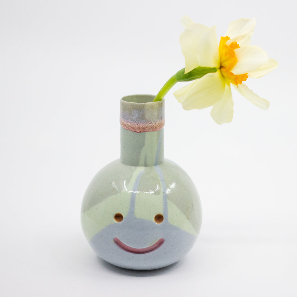 Ceramic vase with a face design holding a yellow flower on a white background