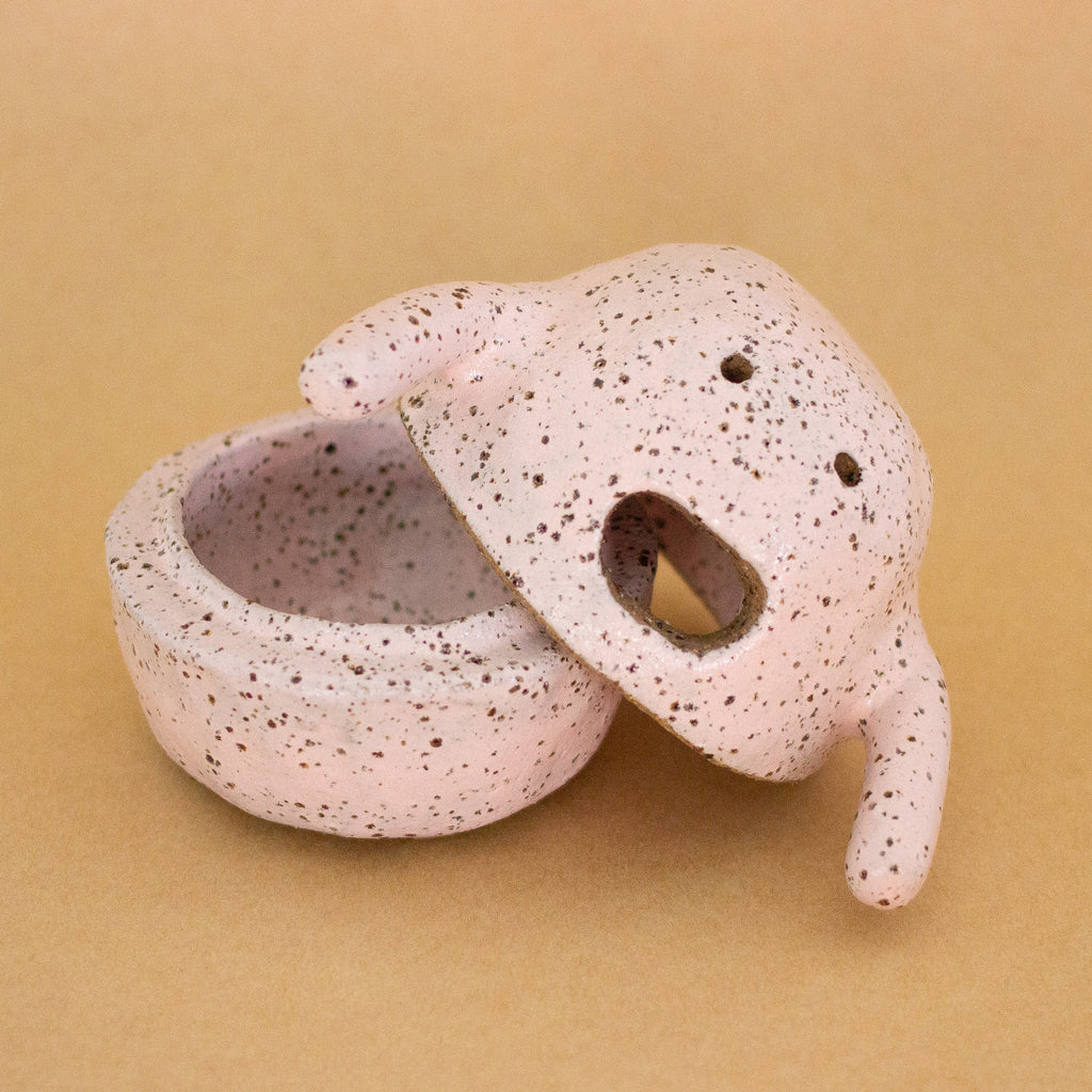 Handbuilt ceramic figurine by shuh. with a speckled pink glaze, round body, small arms, and an open mouth expression. Shows the inside of the bottom canister. 
