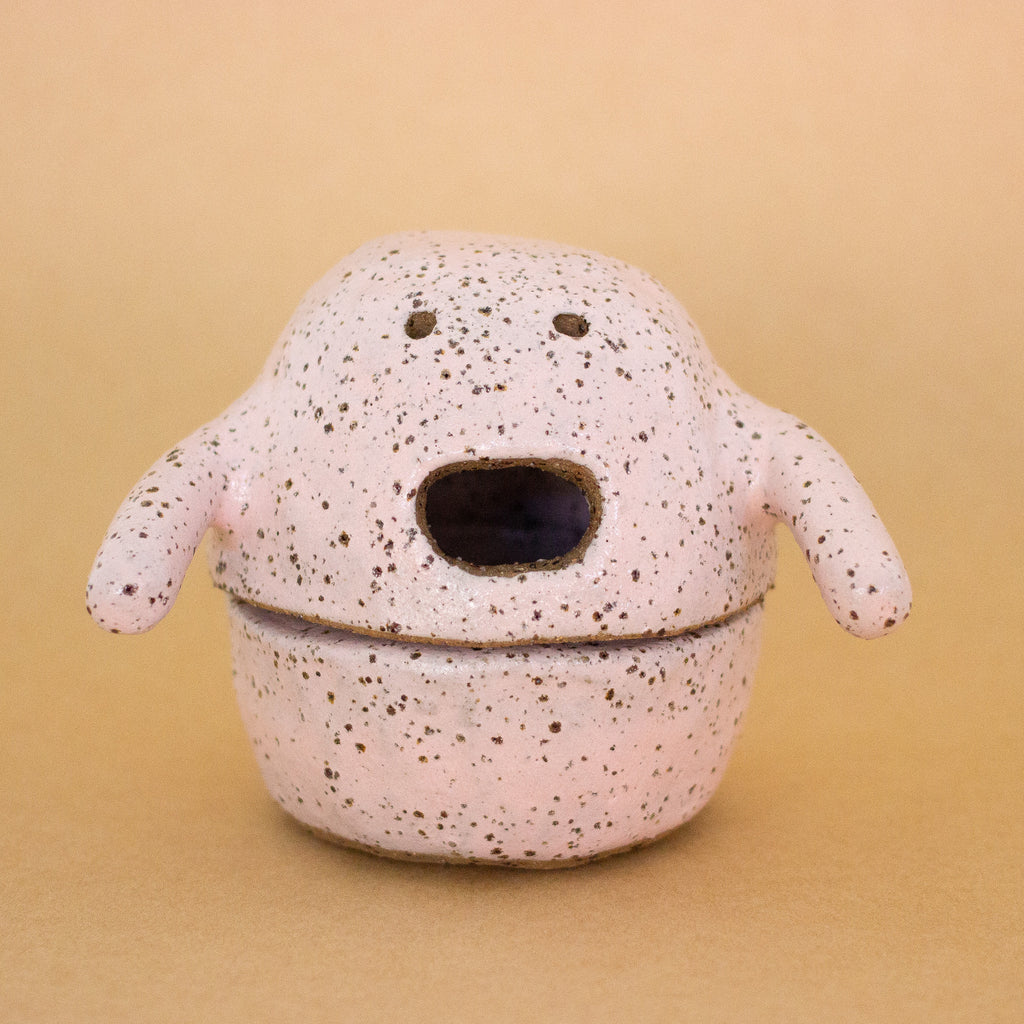 Handbuilt ceramic figurine by shuh. with a speckled pink glaze, round body, small arms, and an open mouth expression.