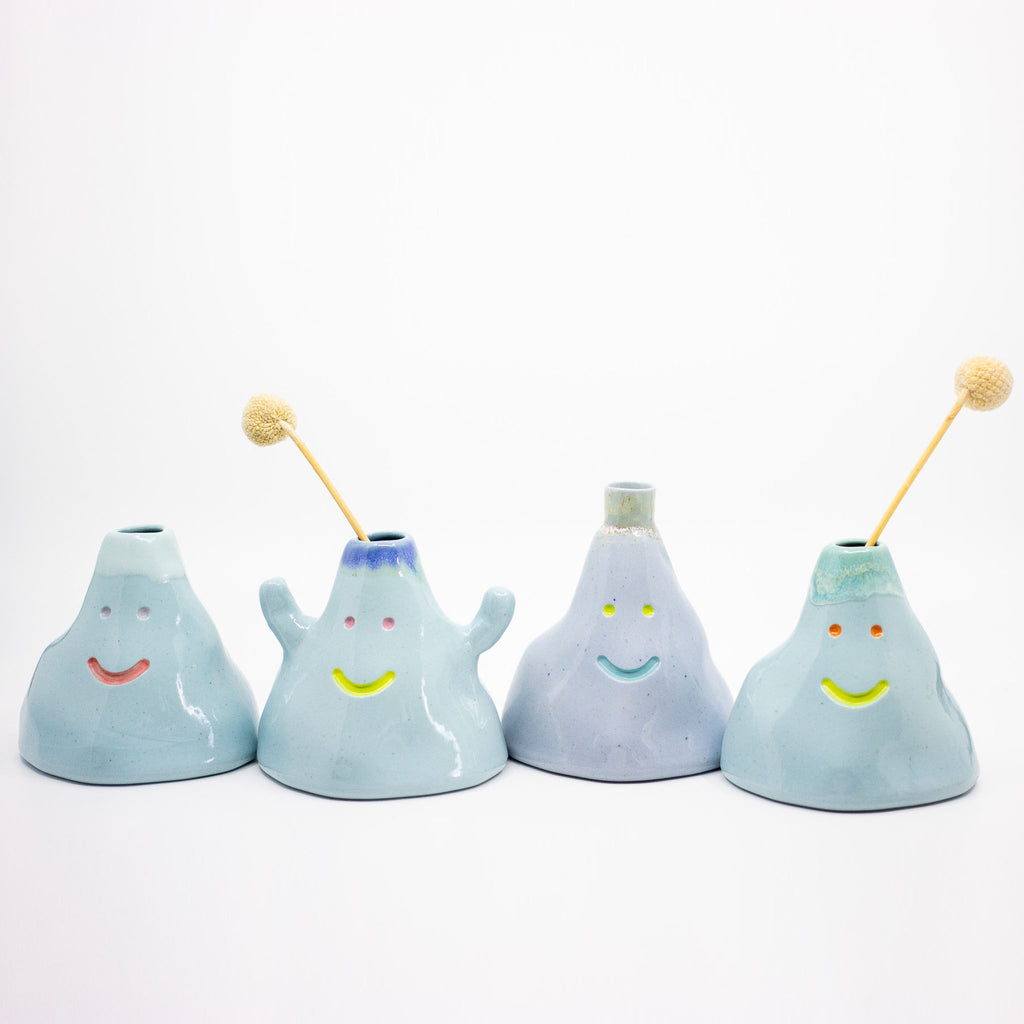 Set of four light blue ceramic vases with smiling faces on a white background