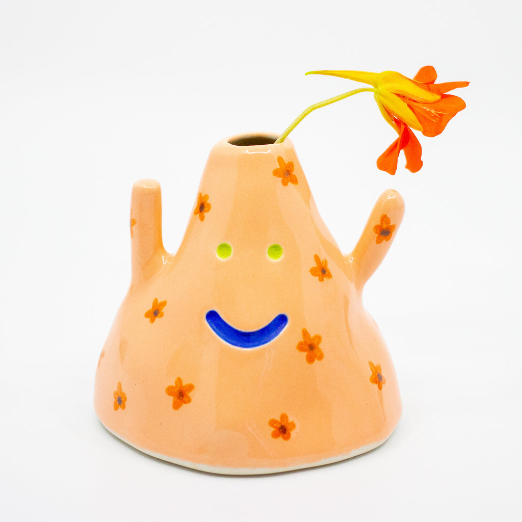 Ceramic vase with a smiley face design and flowers on a white background