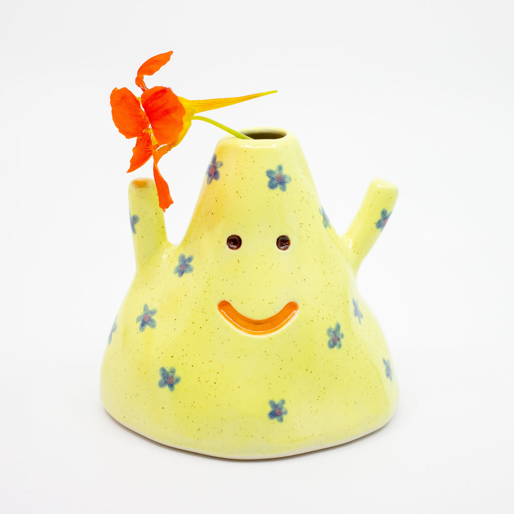 Yellow ceramic vase with a smiley face and floral decorations on a white background