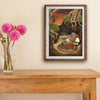 A framed art print depicting a whimsical forest scene with a wombat is displayed on a beige wall above a wooden console table, next to a glass vase with pink flowers.