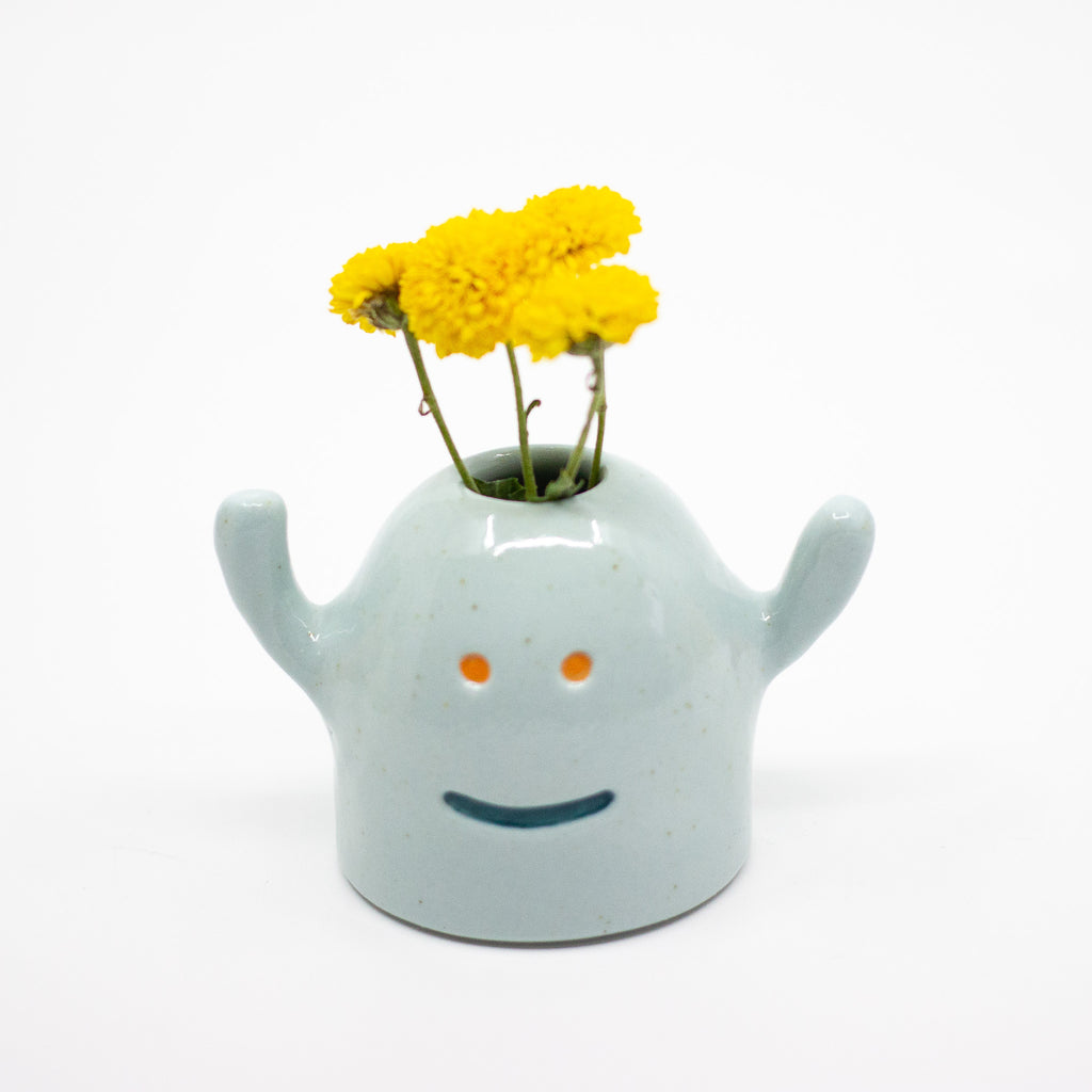 Ceramic vase shaped like a monster with a smiling face with yellow flowers on a white background