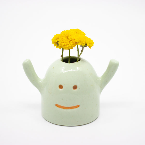 Ceramic monster-shaped vase with yellow flowers on a white background