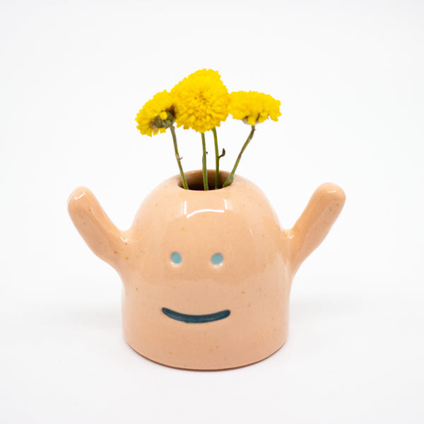 Ceramic vase shaped like a monster with a smiling face with yellow flowers on a white background