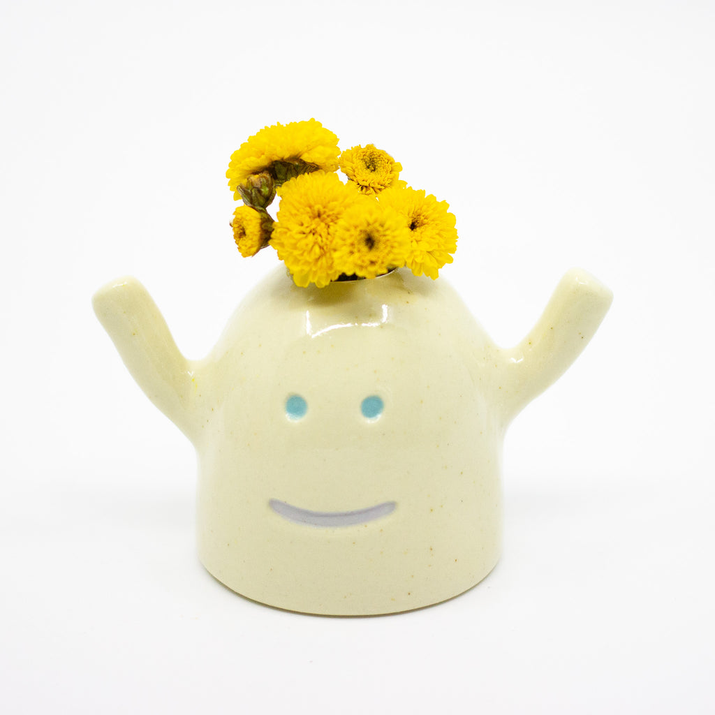 Ceramic monster-shaped vase with yellow flowers on a white background