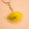 A keychain featuring a yellow lemon-shaped charm with a cute sleeping face and the text 'YOU'RE MY MAIN SQUEEZE' in black, attached to a silver metal keyring, set against a peach background.