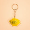 A yellow lemon-shaped keychain with a silver metal split ring and chain, featuring a cute cartoon face and the text 'YOU'RE MY MAIN SQUEEZE' on a peach background.