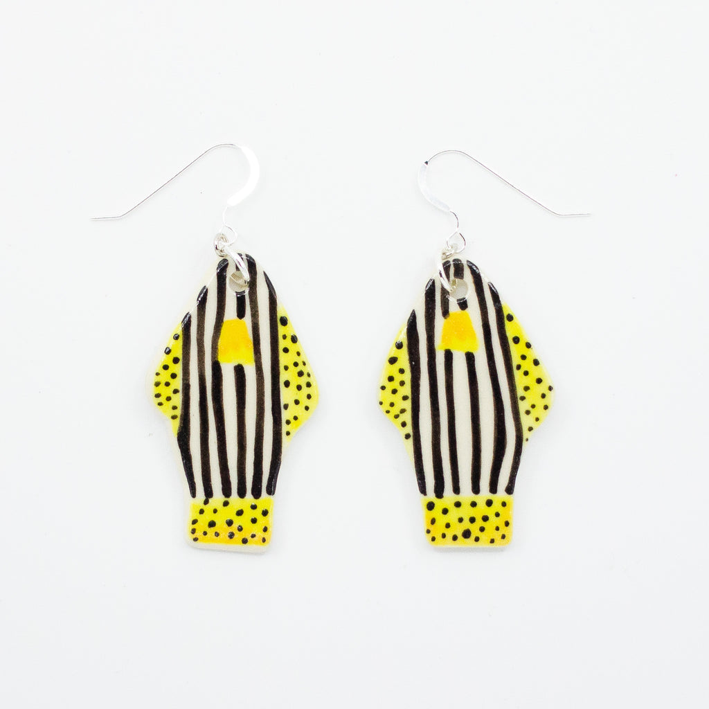 A photo of two ceramic earrings with sterling silver hooks. Earrings are fish shaped, with yellow polka dot fins and tail, and white and black striped body. 