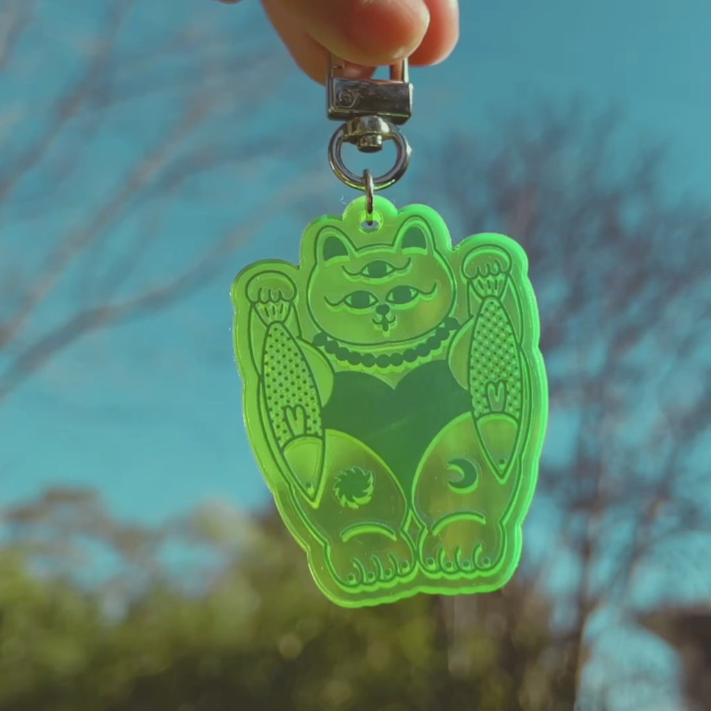A hand holding a neon green cat with third-eye keychain.
