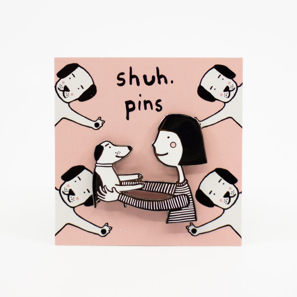 Packaging card with pin. Card is pink, with illustrated dogs. The pin features a girl holding a dog. Girl has pink cheeks. 