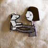 The pin features a girl holding a dog. Girl has pink cheeks. 