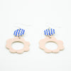 A flat angle of two drop earrings with sterling silver hooks. Each earring has two ceramic pendants, the first is circular with wavy blue handpainted lines. The second is a larger circular pendant with pink colour and flower shape. 