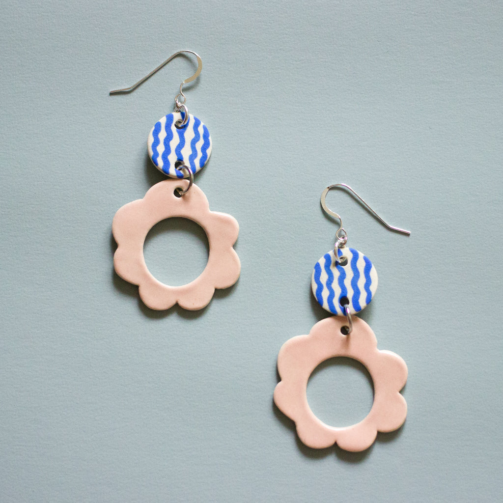 Two drop earrings with sterling silver hooks. Each earring has two ceramic pendants, the first is circular with wavy blue handpainted lines. The second is a larger circular pendant with pink colour and flower shape. 
