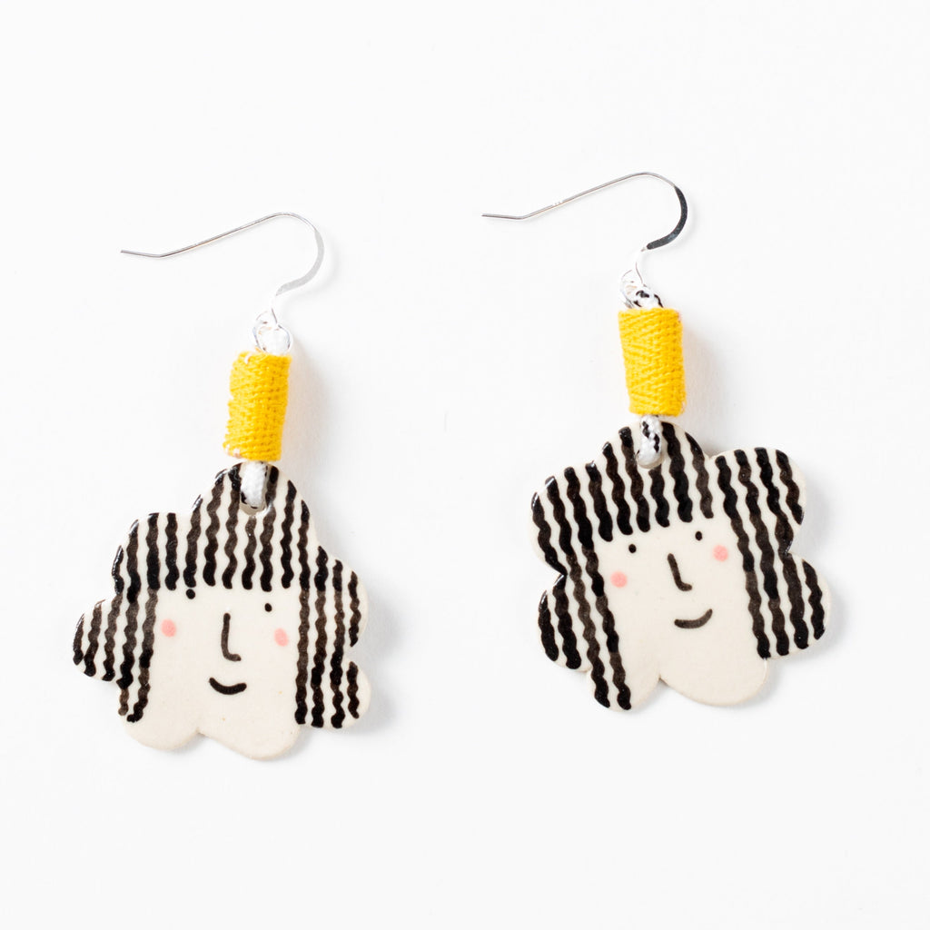 Two drop earrings with short hooks, and yellow fabric accents. Ceramic beads with girls face, a smile, pink cheeks, and curly hair. 