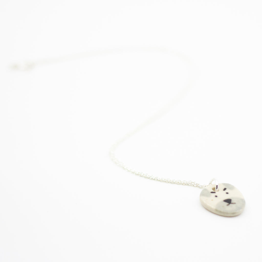 Sterling silver necklace featuring a round ceramic pendant hand-painted with a light grey and cream dog face, including expressive eyebrows and a small brown mouth, displayed on a white background.