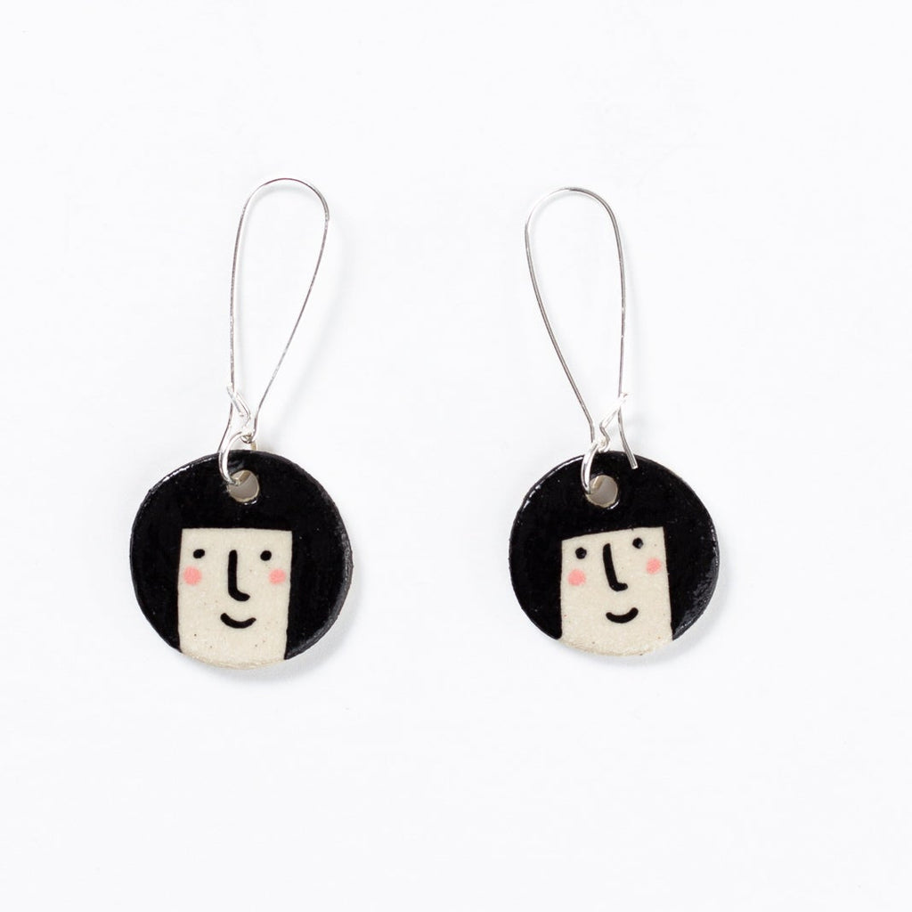 Two ceramic drop earrings with sterling silver hooks. Pendant is circular with a girls face and bob hair. Pink cheeks with a pleasant smile. 