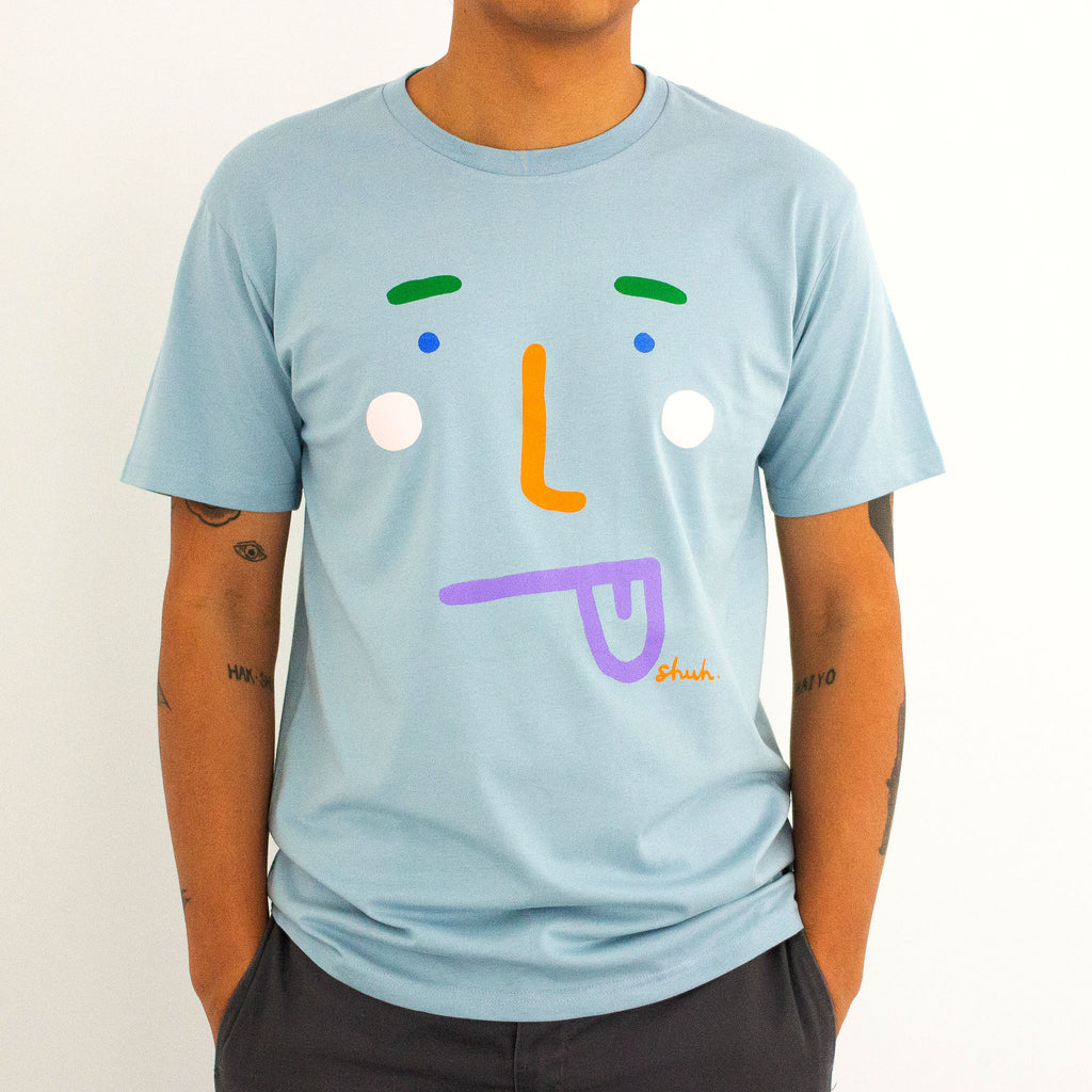 A model wearing the boo tee. Blue coloured tee, with a stylised face with tongue poking out. 
