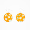 A pair of handmade ceramic earrings with round orange drops, decorated with a pattern of white flowers and green centres. Finished with silver hooks for pierced ears.