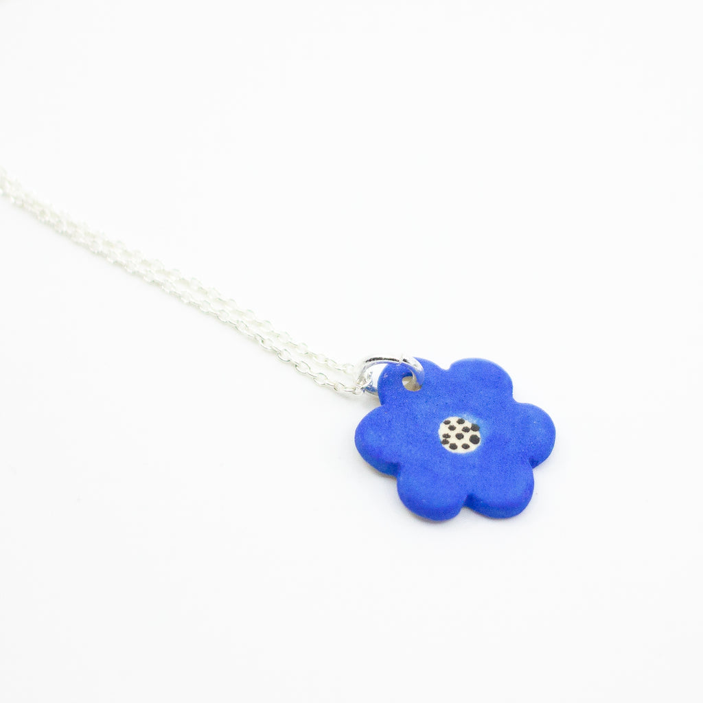 Sterling silver necklace featuring a bright blue ceramic flower-shaped pendant with a polkadot pattern in the centre, displayed on a white background.