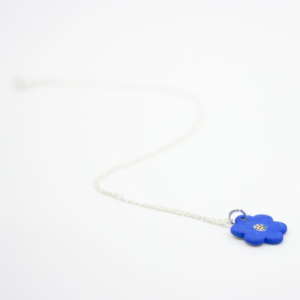 Sterling silver necklace featuring a bright blue ceramic flower-shaped pendant with a polkadot pattern in the centre, displayed on a white background.