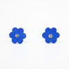 A pair of handmade ceramic stud earrings shaped like bright blue flowers with speckled cream and black centres. Finished with sterling silver stud backings for pierced ears.