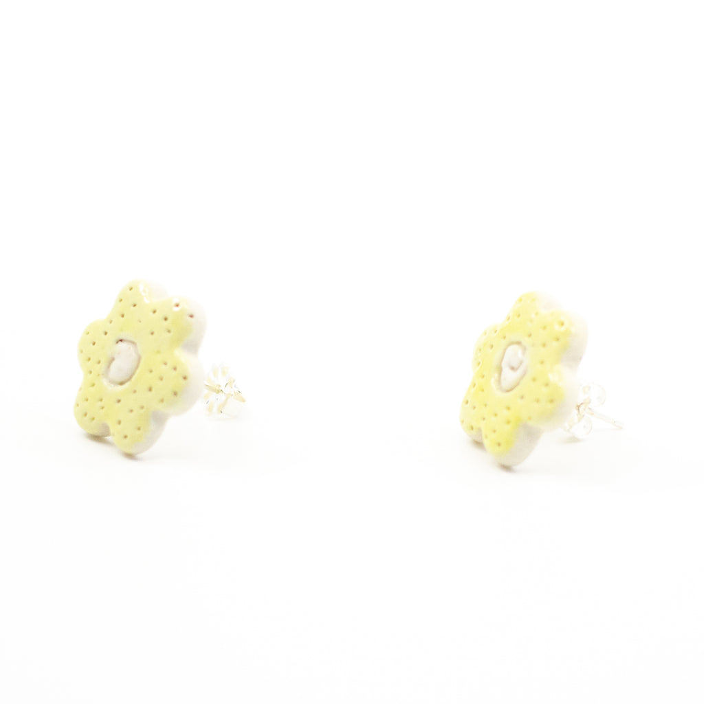 Side view of a pair of handmade ceramic stud earrings shaped like small yellow buttercup flowers, with tiny dotted details and a carved centre. Finished with sterling silver posts.