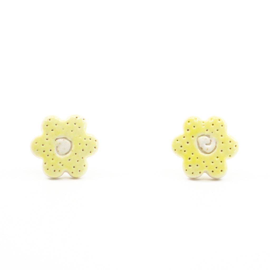 A pair of handmade ceramic stud earrings shaped like small yellow buttercup flowers, with tiny dotted details and a carved centre. Finished with sterling silver posts.