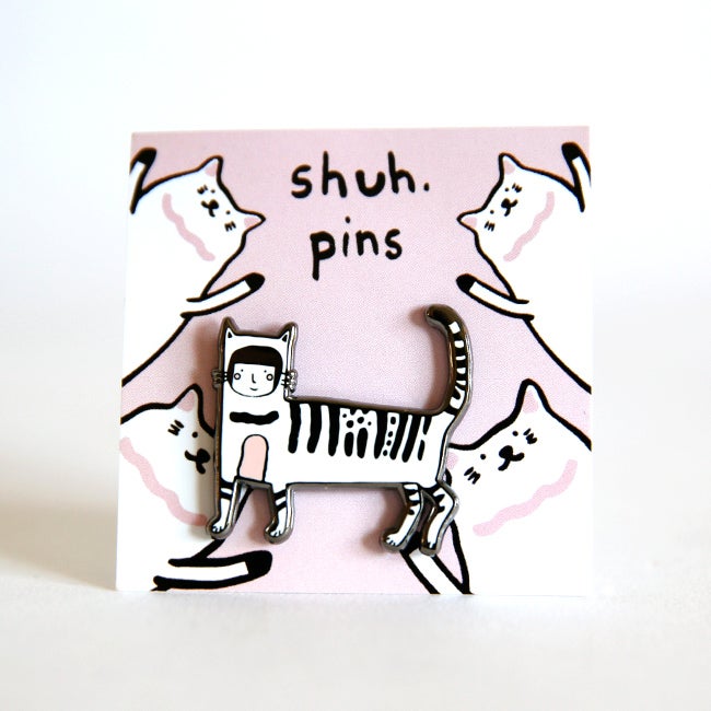 Enamel pin of a hand-drawn person dressed in a full-body cat suit, displayed on a pink card with cat illustrations and “shuh. pins” branding.