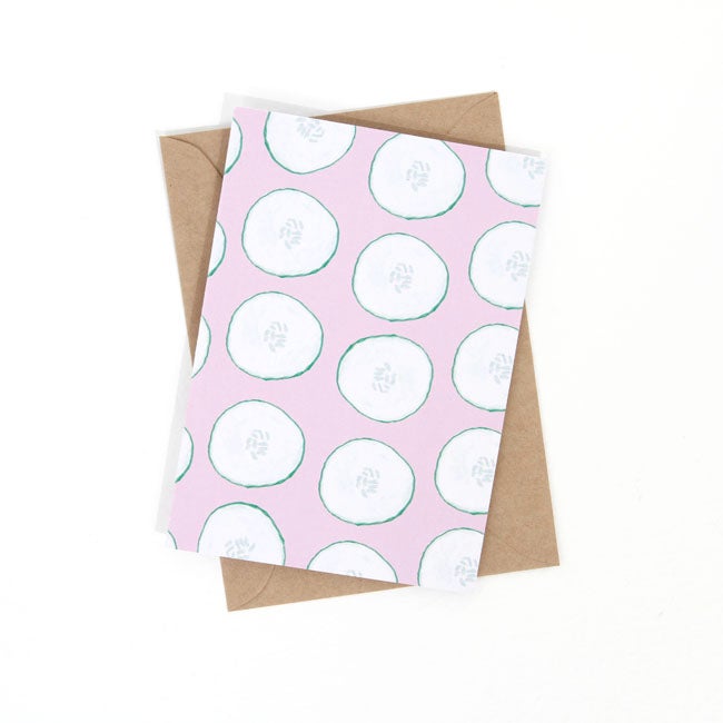 Front view of the cool as a cucumber print. Repeated cucumber slices over a pink background. 